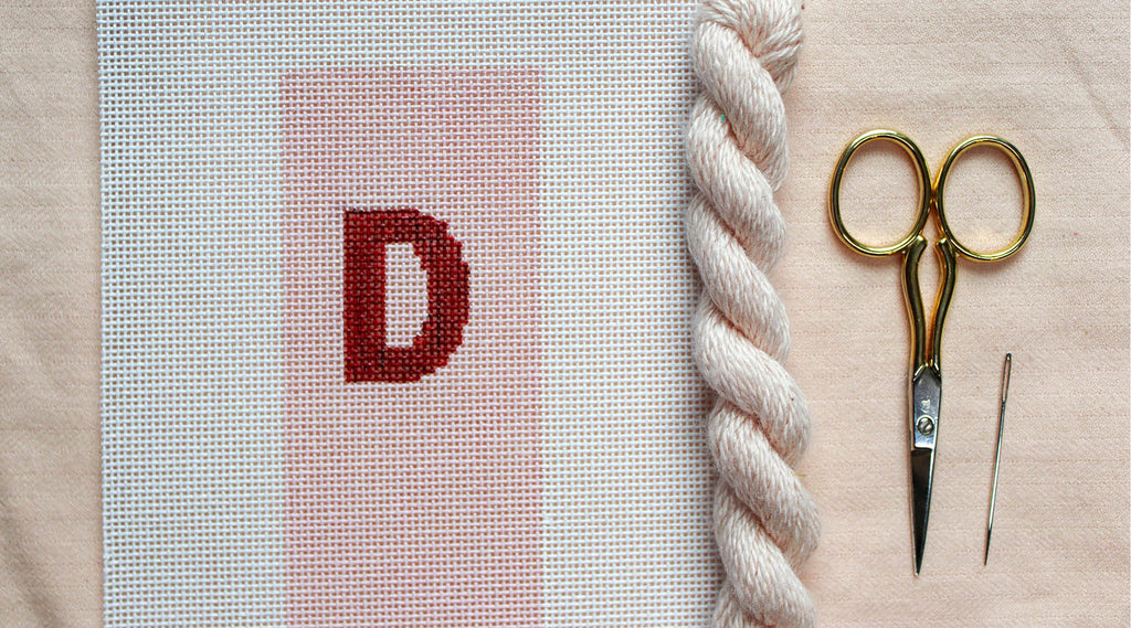 Flat lay of beginner needlepoint supplies including canvas, thread, needle, embroidery scissors, and canvas, ready for a needlepoint project.